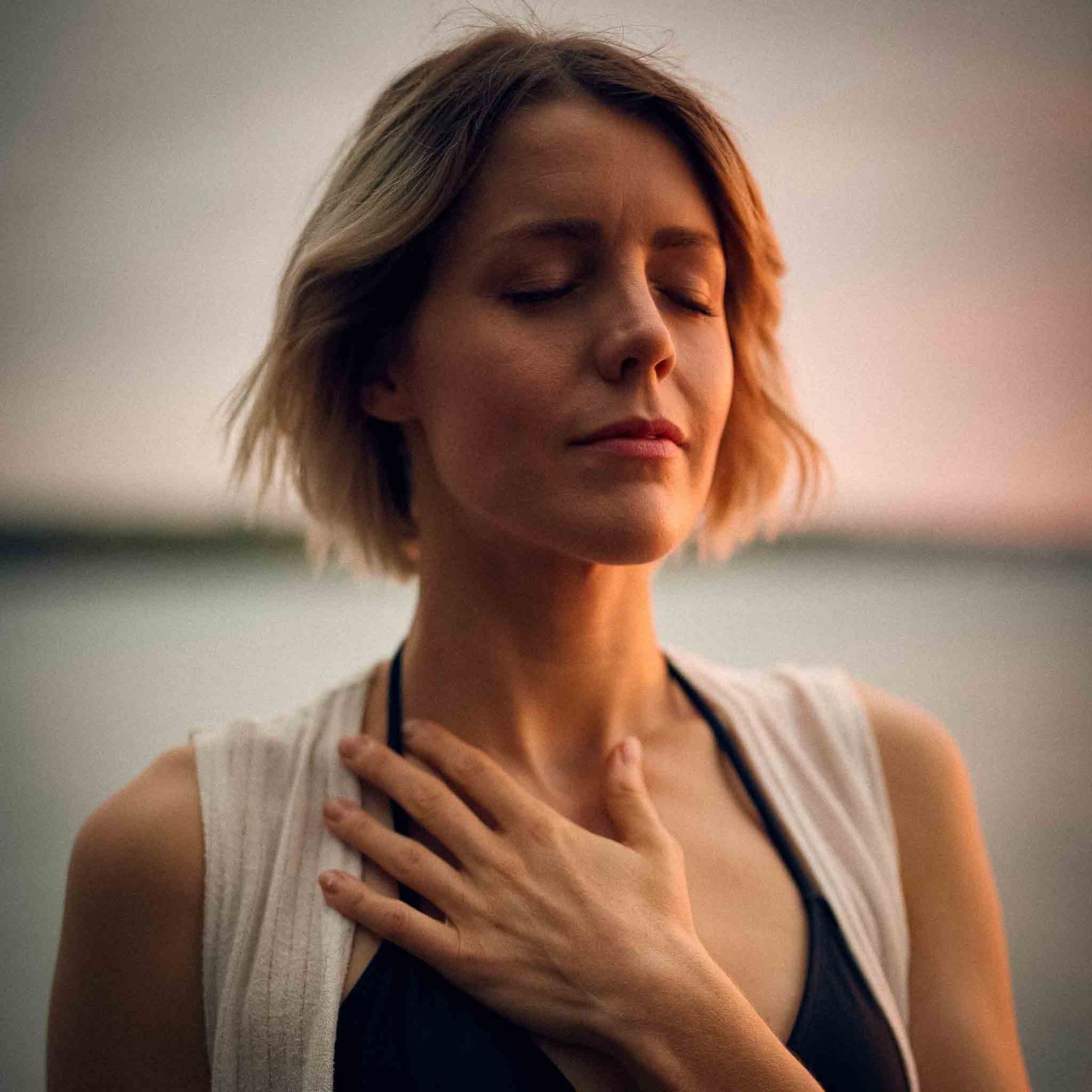 Image taken by Darius Bashar. A woman standing peacefully with her hand over her heart space. Calm and grateful.