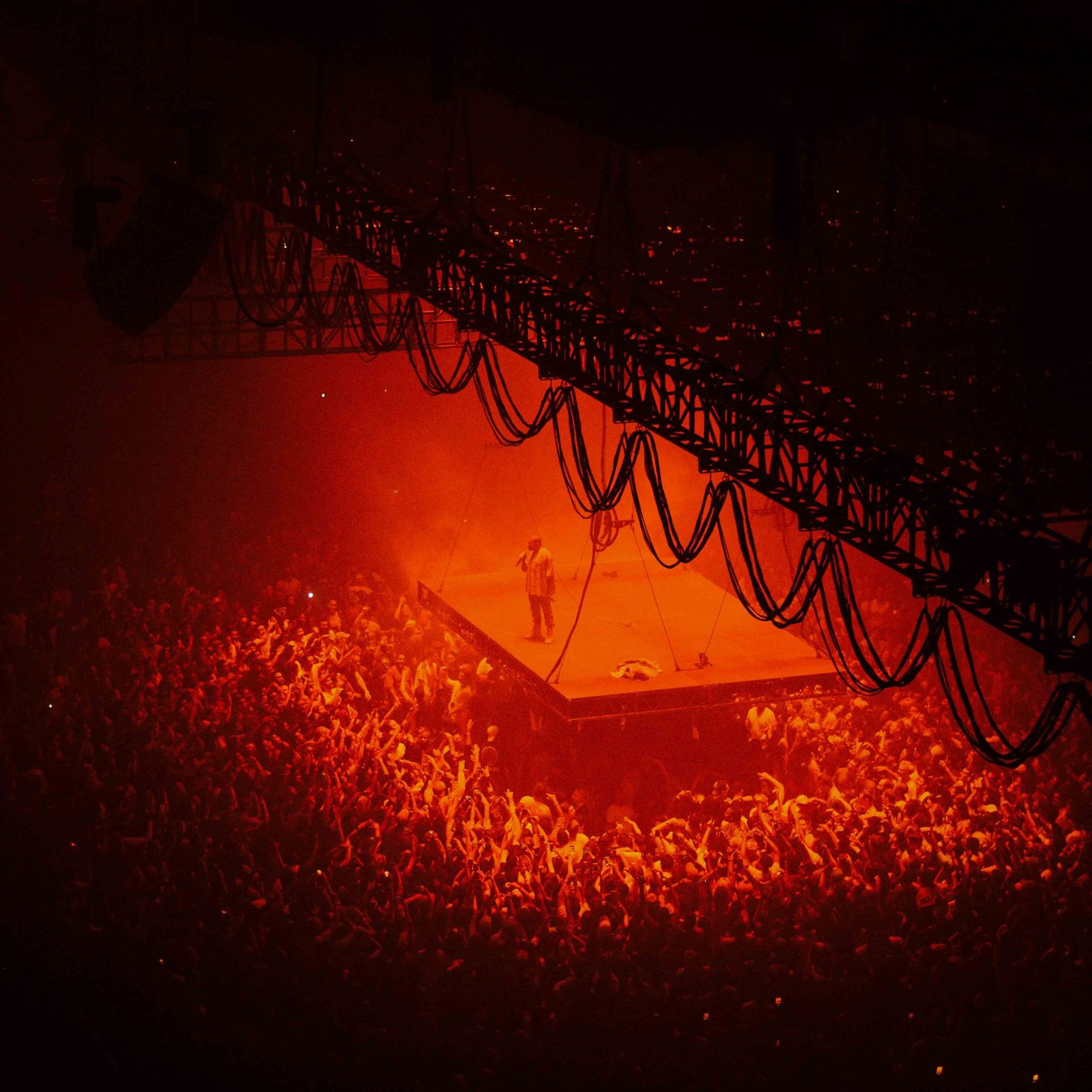 Kanye West performing on a suspended stage in-front of thousands of people.